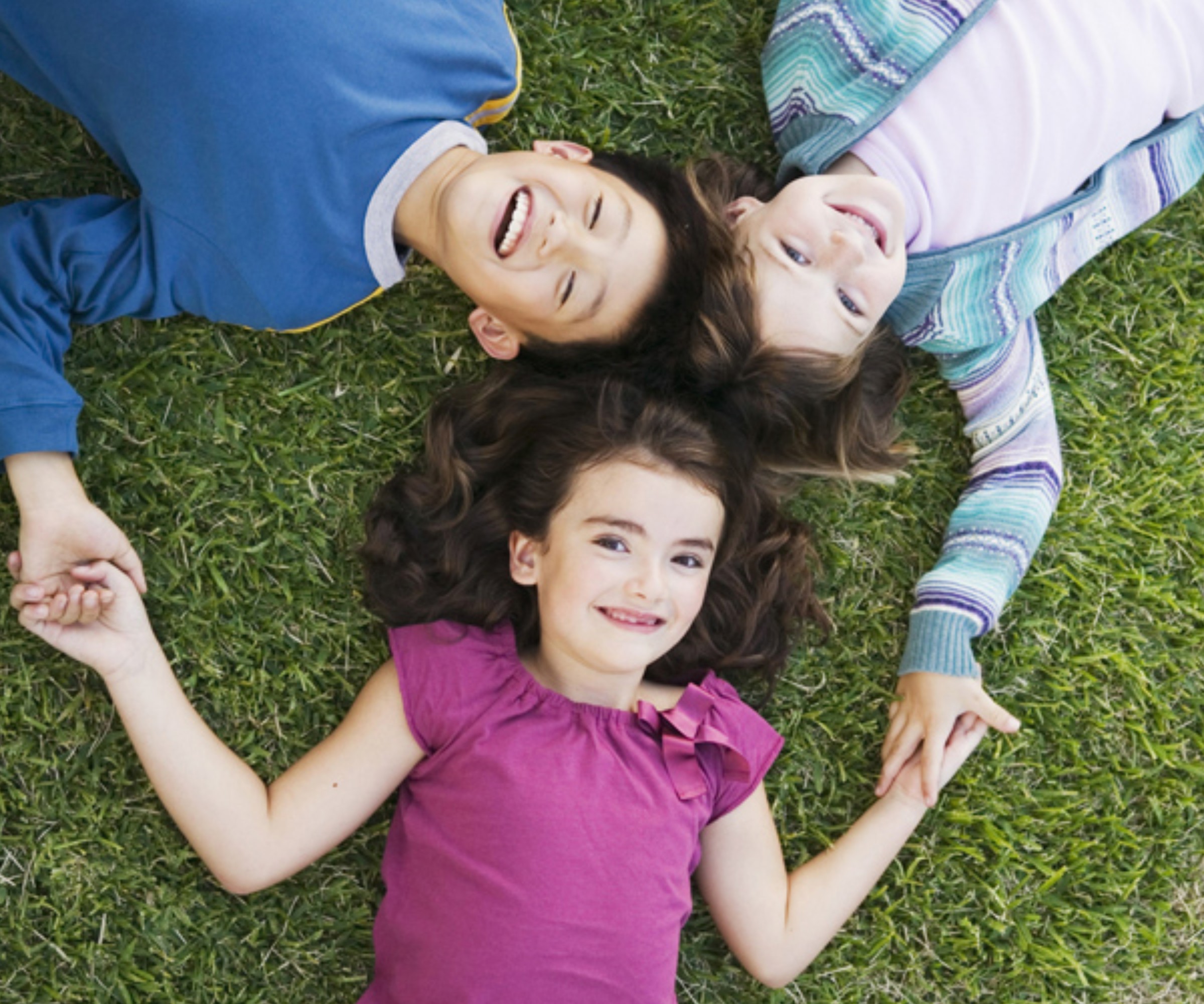 Treatments for the Whole Family 3 kids laying on grass and looking up while smiling happily